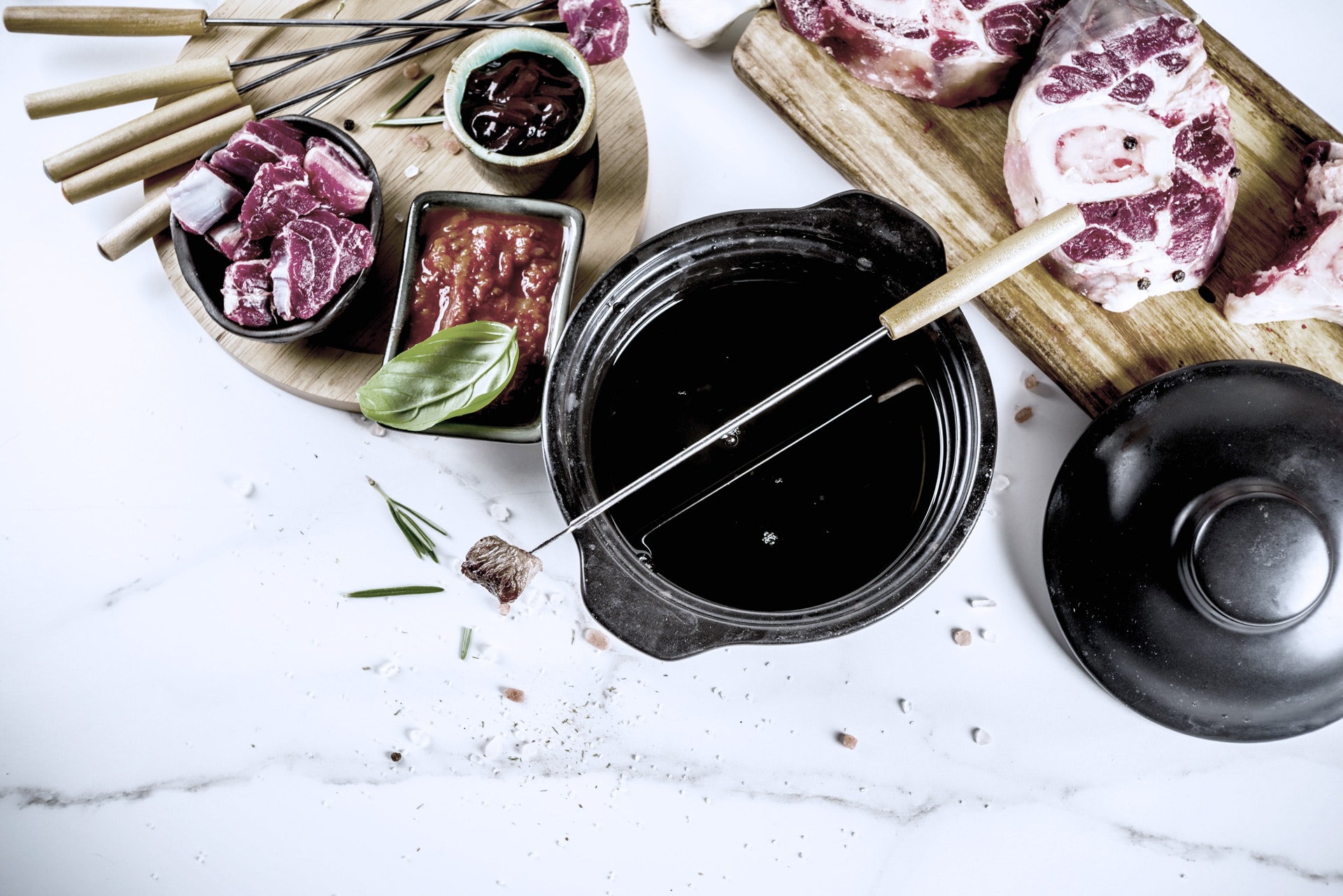 fondue Ein Gourmet-Hotpot mit verschiedenen rohen Fleischstücken, Dip-Saucen und Stäbchen, elegant auf einer Marmorplatte angerichtet.