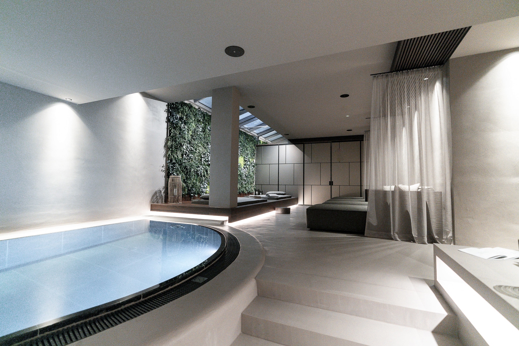 Wellness - Entspannung Ein ruhiger und moderner Spa-Bereich im Innenbereich mit einem eleganten blauen Pool, Stufen, die zu einem entspannenden Loungebereich führen, und einer mit Grünpflanzen geschmückten Wand, die eine Oase der Ruhe schafft.